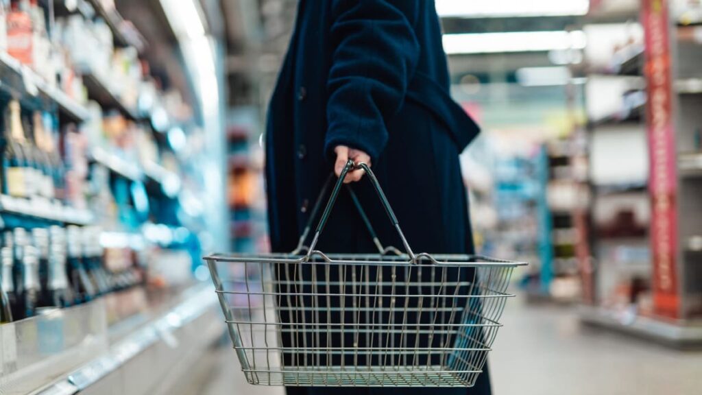 Žena s nákupním košíkem v uličce supermarketu — nákupy před Velikonocemi